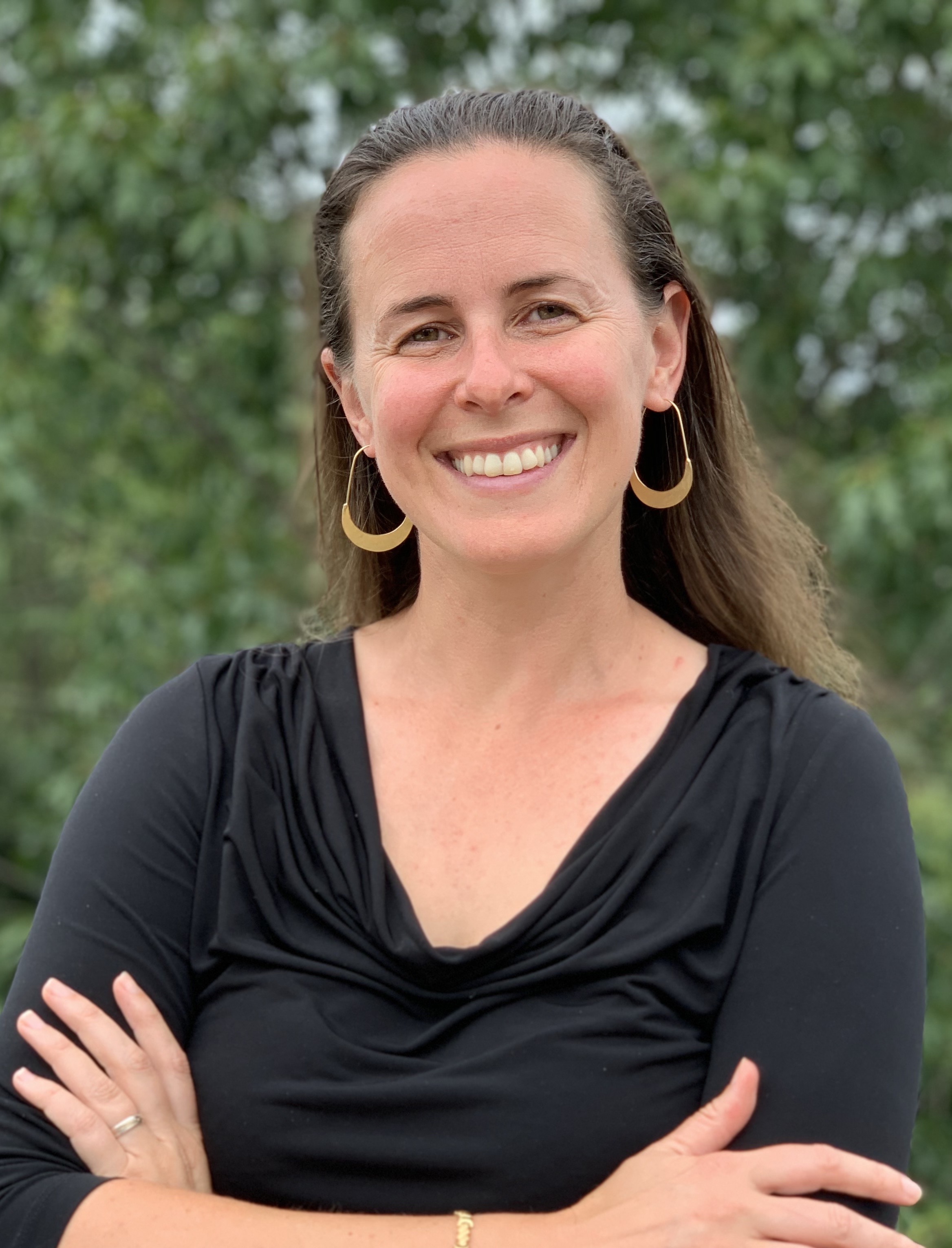 A person smiling with her arms crossedDescription automatically generated